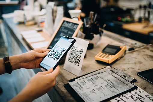 Customer scanning QR code, making a quick and easy contactless payment with her smartphone in a cafe.