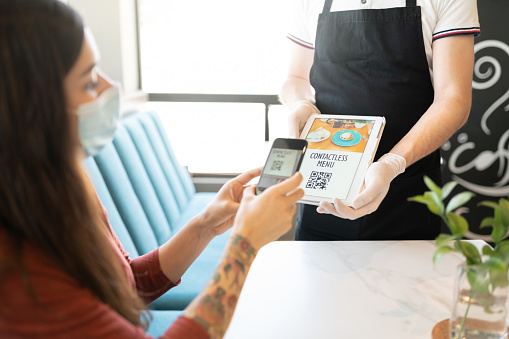 Young woman scanning QR code of contactless menu through the smartphone in a restaurant.